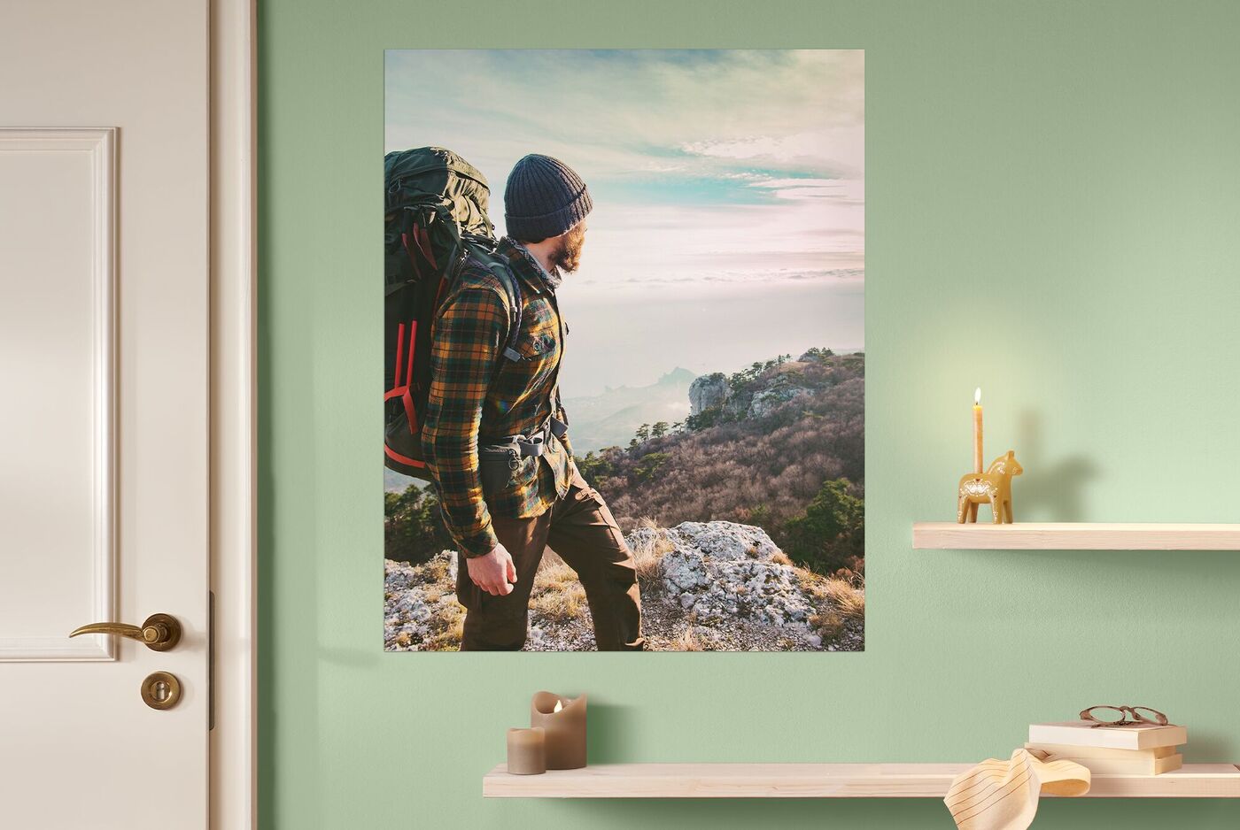 CEWE Wandbild mit Foto eines Wanderers auf Felsen, der in die Ferne schaut, im Raum mit grüner Wand und dekorativen Regalen