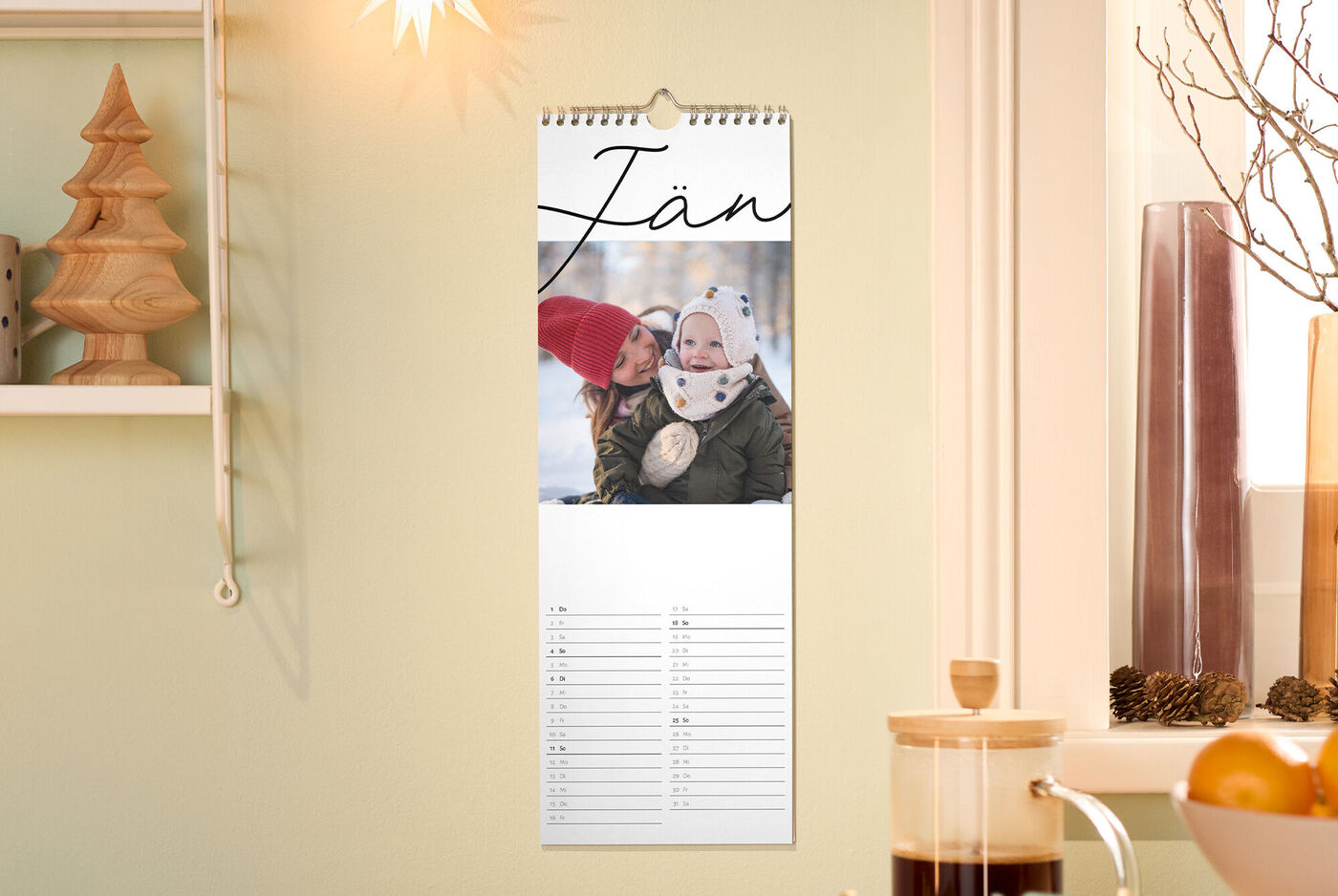 Küchenkalender im Monat „Jänner“ mit liebevollem Winterfoto, warmem Sternenlicht, Holzbaumdeko und Tannenzapfen am Fenster.