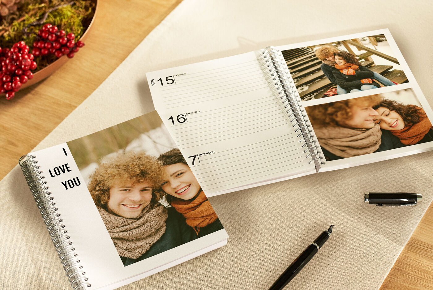 Weihnachtliche Gemütlichkeit: Zwei Terminplaner mit liebevollen Paarfotos auf dem Tisch, rote Beeren – ein Geschenk von Herzen.