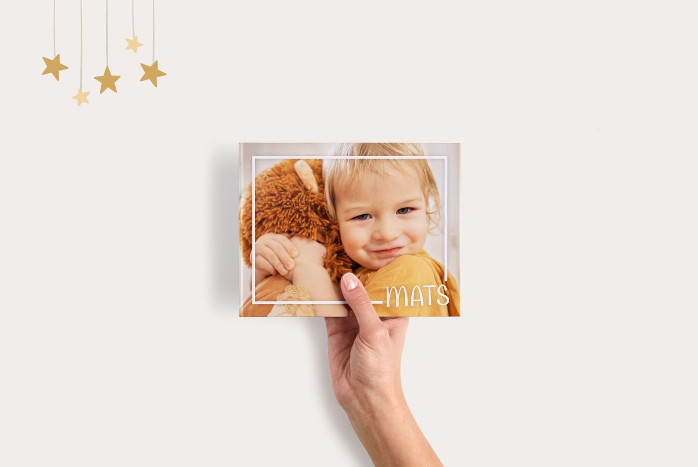 Hand hält ein CEWE FOTOBUCH Compact Panorama mit Kind und Teddybär auf dem Cover, minimalistischer Rahmen um das Foto