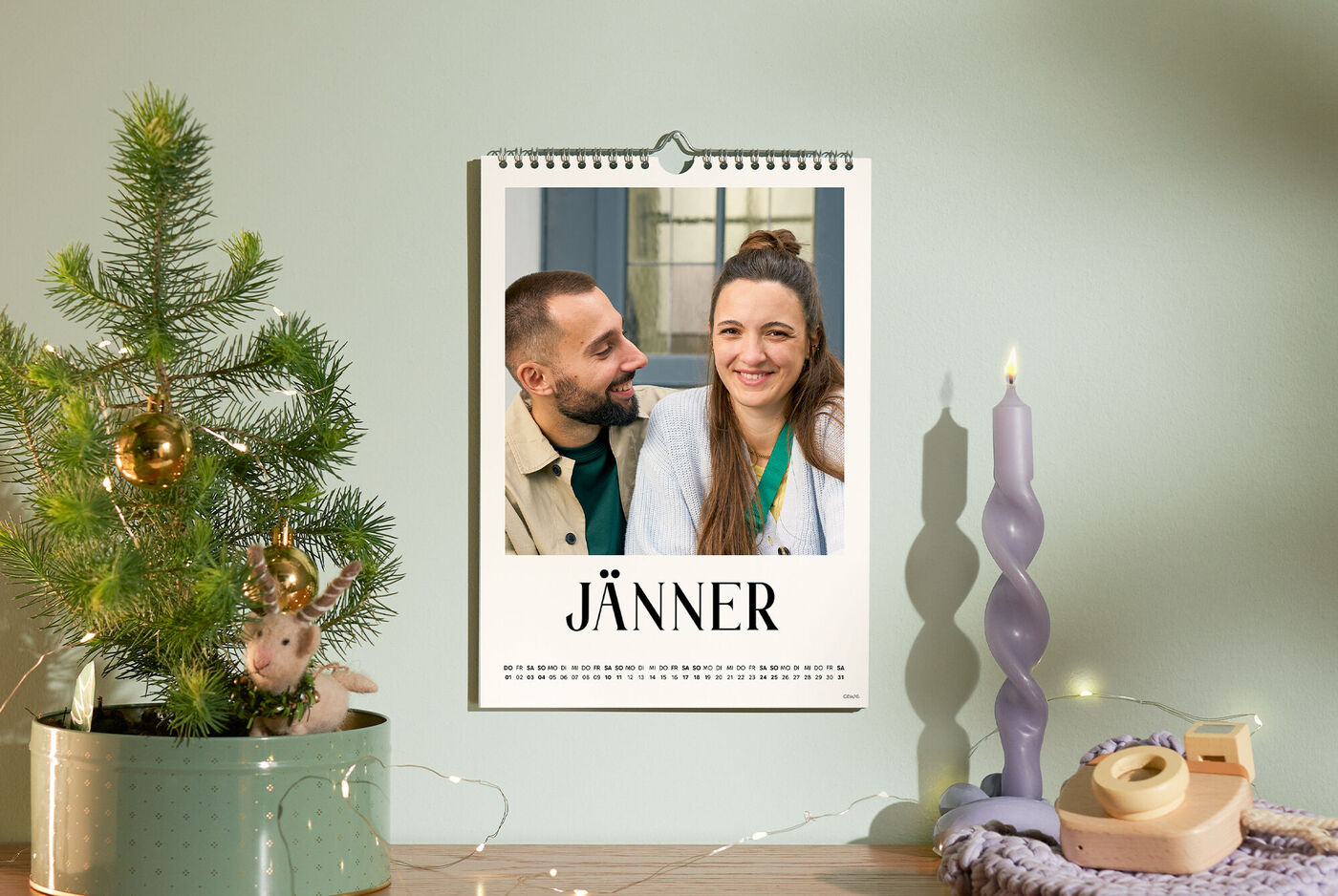 CEWE Fotokalender an grüner Wand mit Paarfoto, Monat Jänner, Deko mit Baum und Kerze