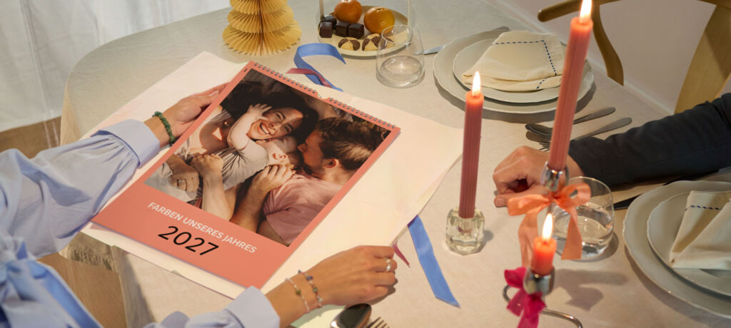 Zwei Personen am festlich gedeckten Tisch betrachten einen CEWE Fotokalender mit Familienfoto und Jahreszahl 2026