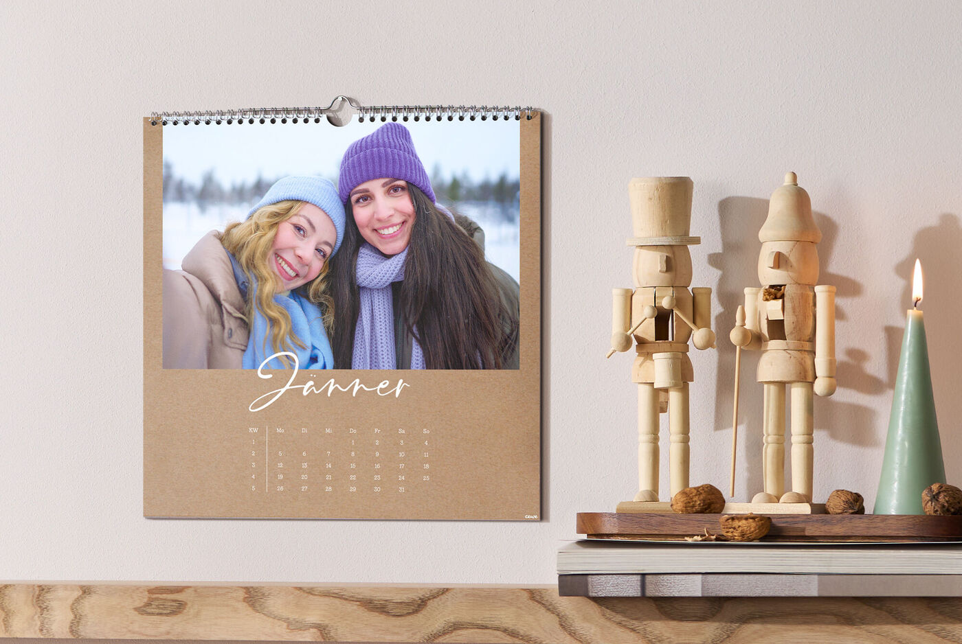 CEWE Fotokalender auf Regal mit zwei Holzfiguren daneben, Winterfoto von zwei Personen, Monat Jänner