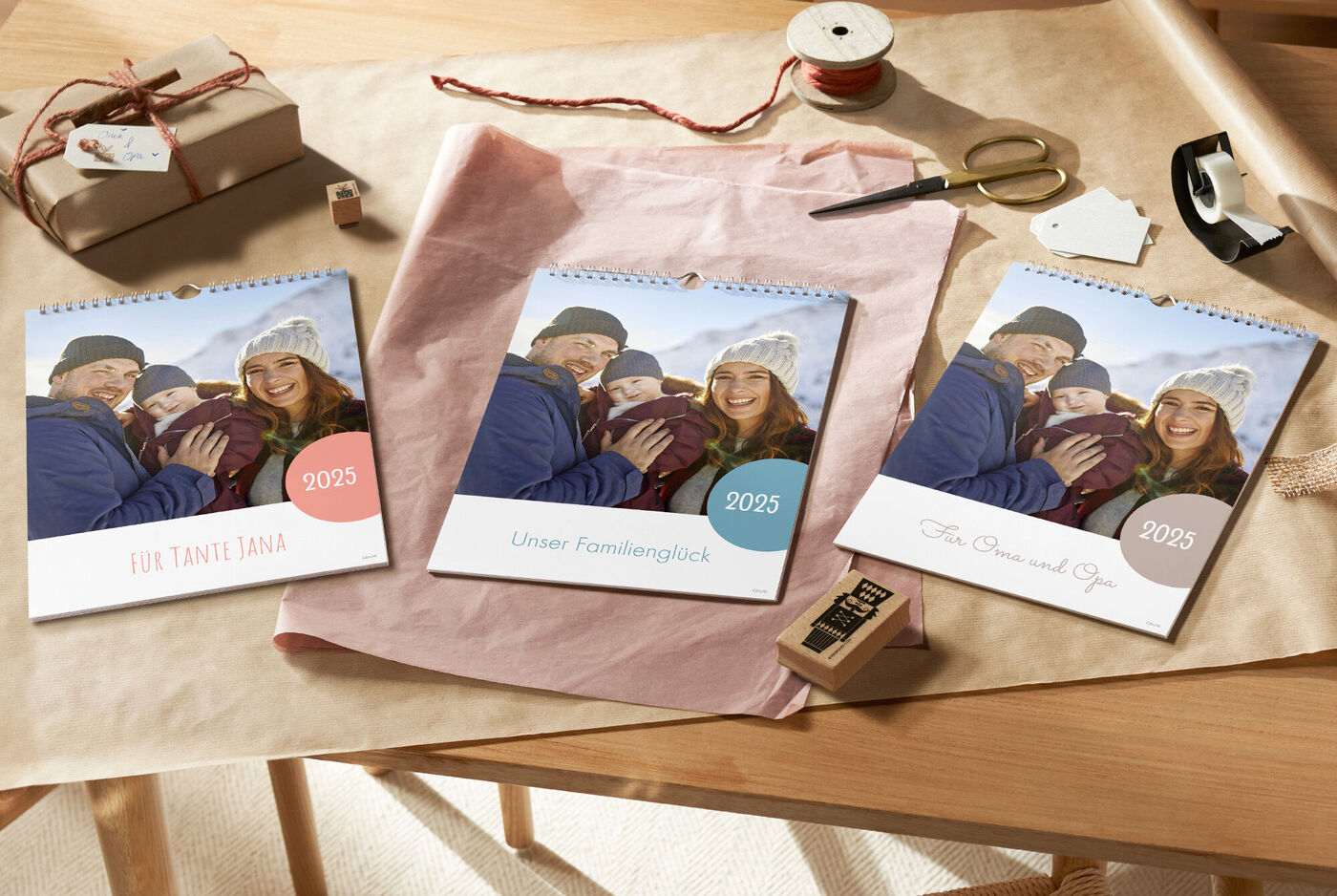 Zwei glückliche Personen halten einen CEWE Fotokalender in den Händen, während sie auf einem Tisch mit Geschenkpapier und Bastelmaterialien sitzen