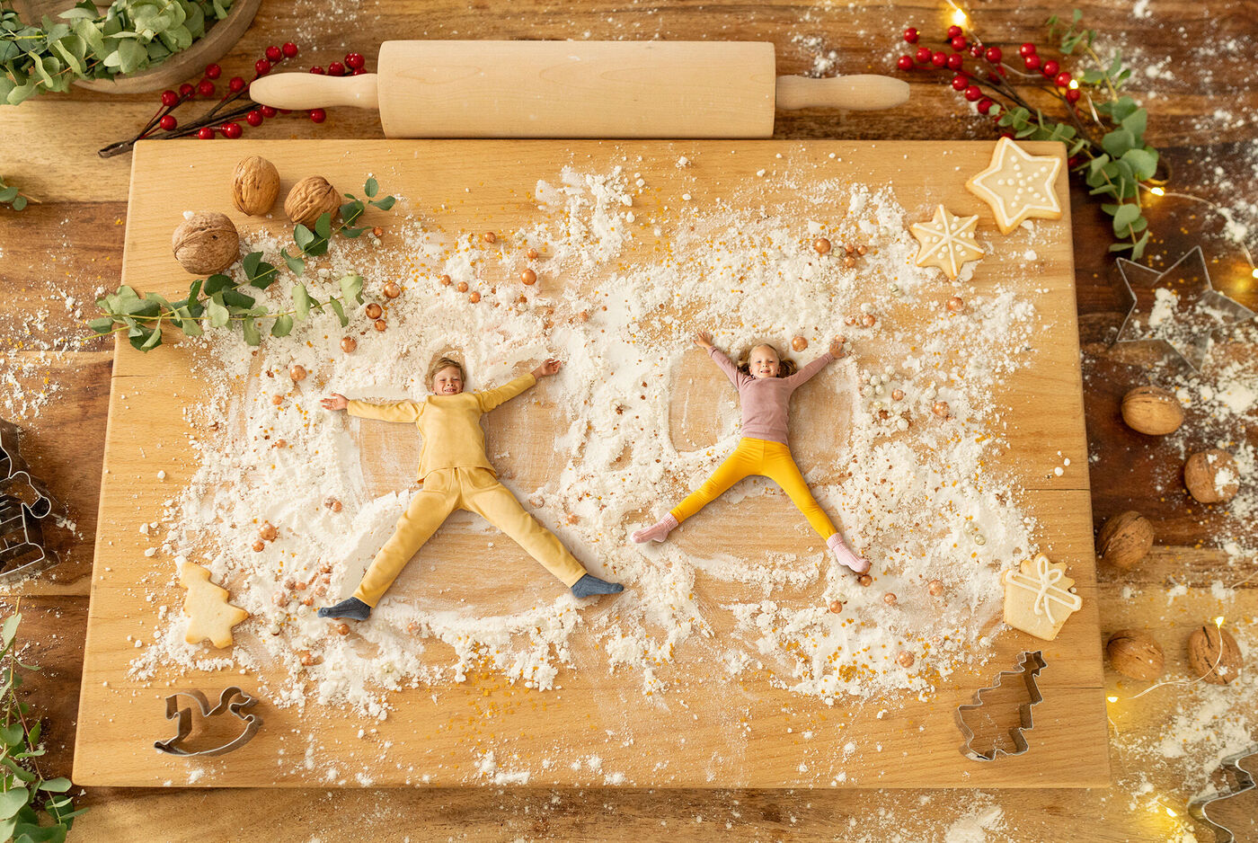 Zwei Figuren aus Teig liegen auf einem Holzbrett mit Mehl und Weihnachtsdekoration, die eine fröhliche Stimmung ausstrahlen