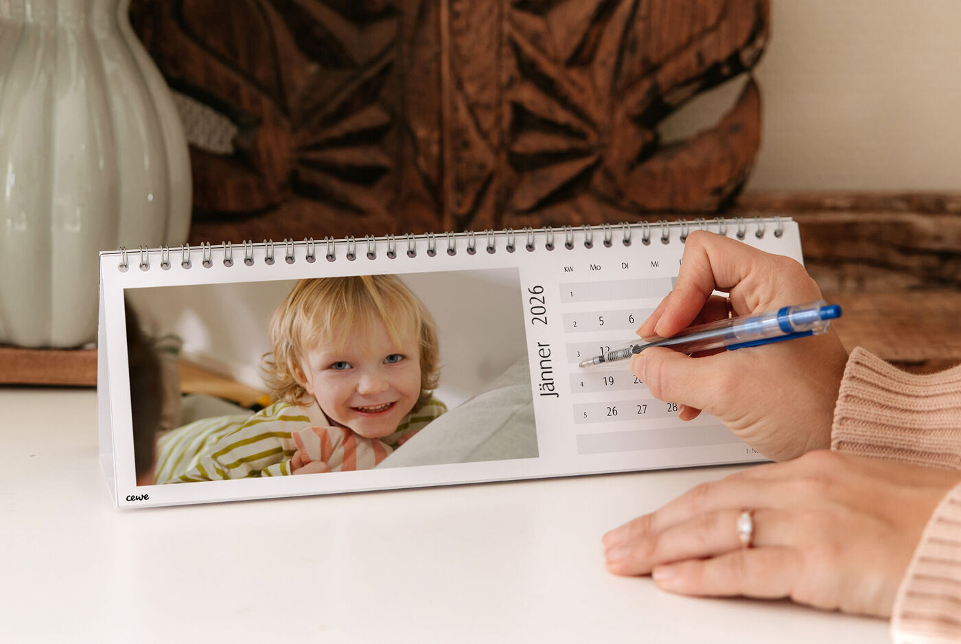 Ein CEWE Fotokalender auf einem Tisch zeigt ein lächelndes Mädchen im Bett