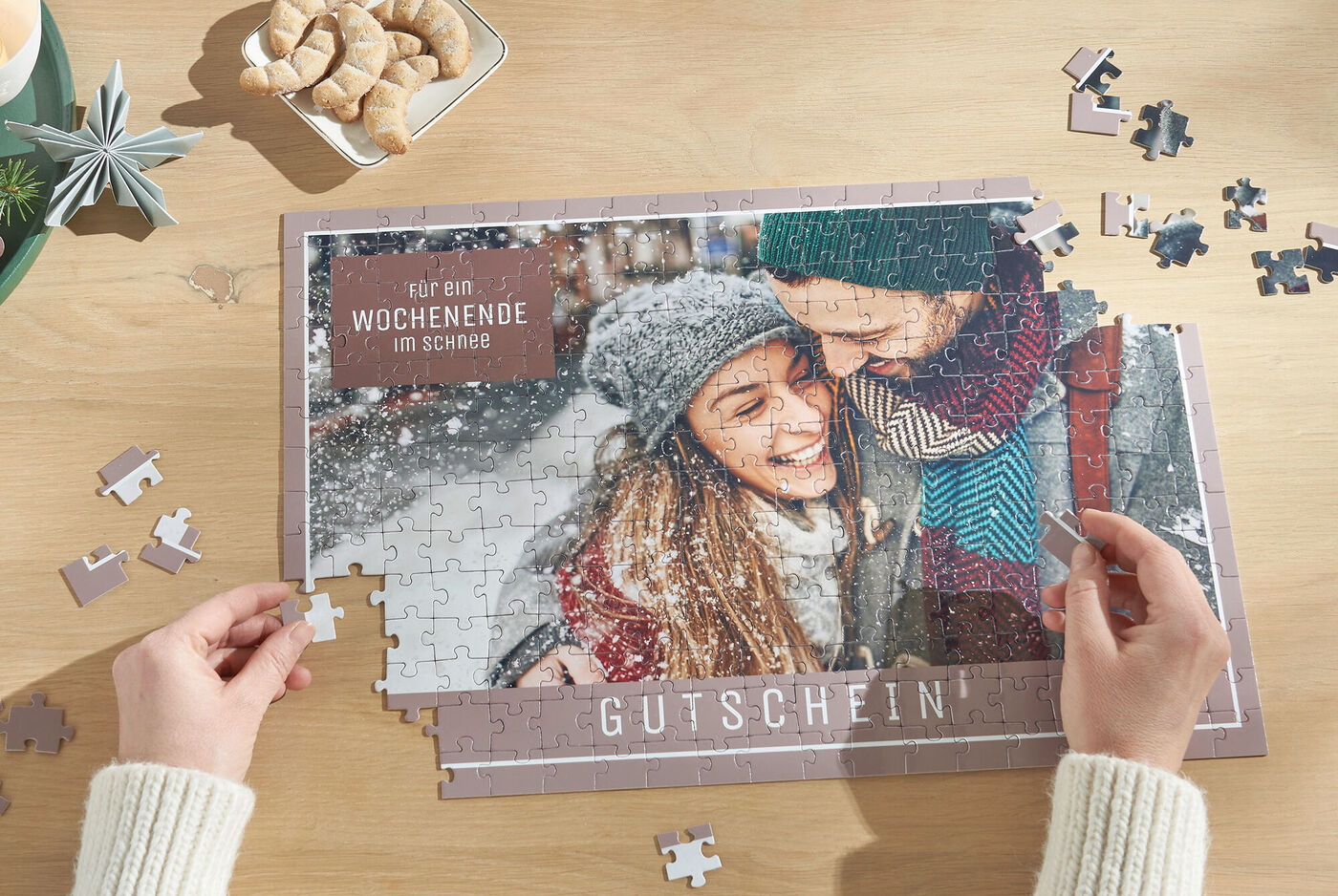 Zwei Personen setzen gemeinsam ein Puzzle zusammen mit einem Gutschein für ein Wochenende im Schnee
