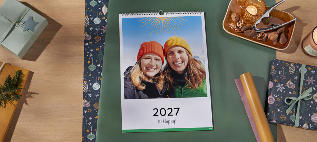 Ein fröhlicher Kalender für 2025 mit zwei Personen in farbenfrohen Mützen, umgeben von festlicher Dekoration