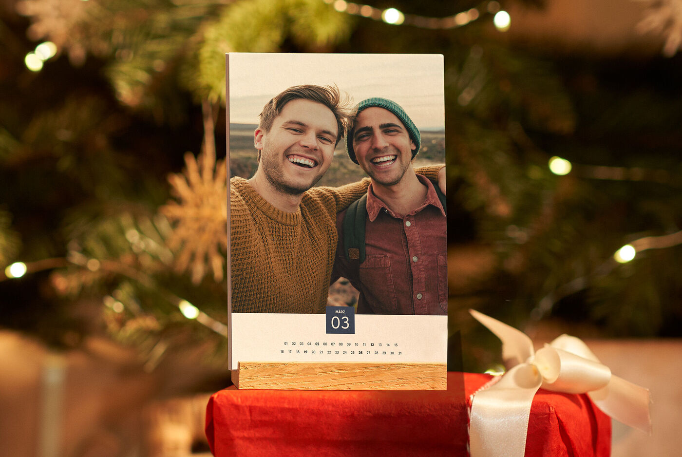 Ein schöner Kalender mit einem persönlichen Foto von zwei Freunden, die glücklich in die Kamera lächeln. Der Kalender steht auf einem Tisch, umgeben von Weihnachtsdekoration.