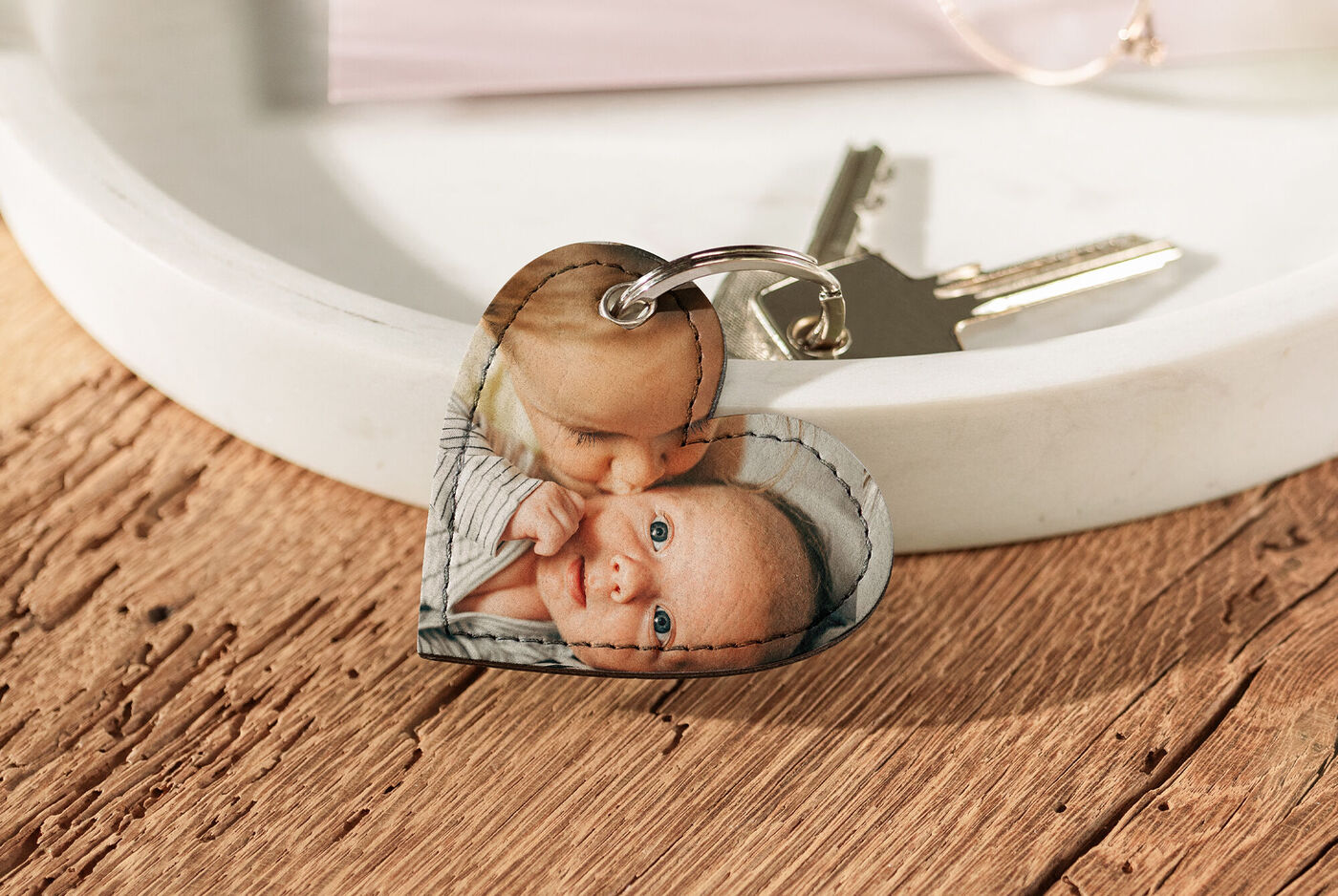Ein herzförmiger Schlüsselanhänger mit einem Bild von einem Baby. Der Schlüsselbund liegt auf einer Holzoberfläche.