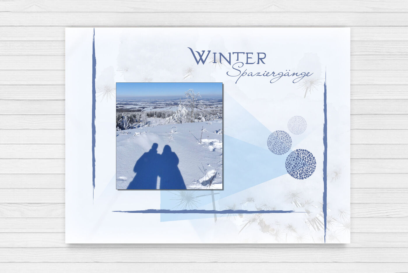 Pärchen im Schatten auf verschneiter Winterlandschaft, umgeben von blauen Akzenten und winterlicher Dekoration. CEWE FOTOBUCH