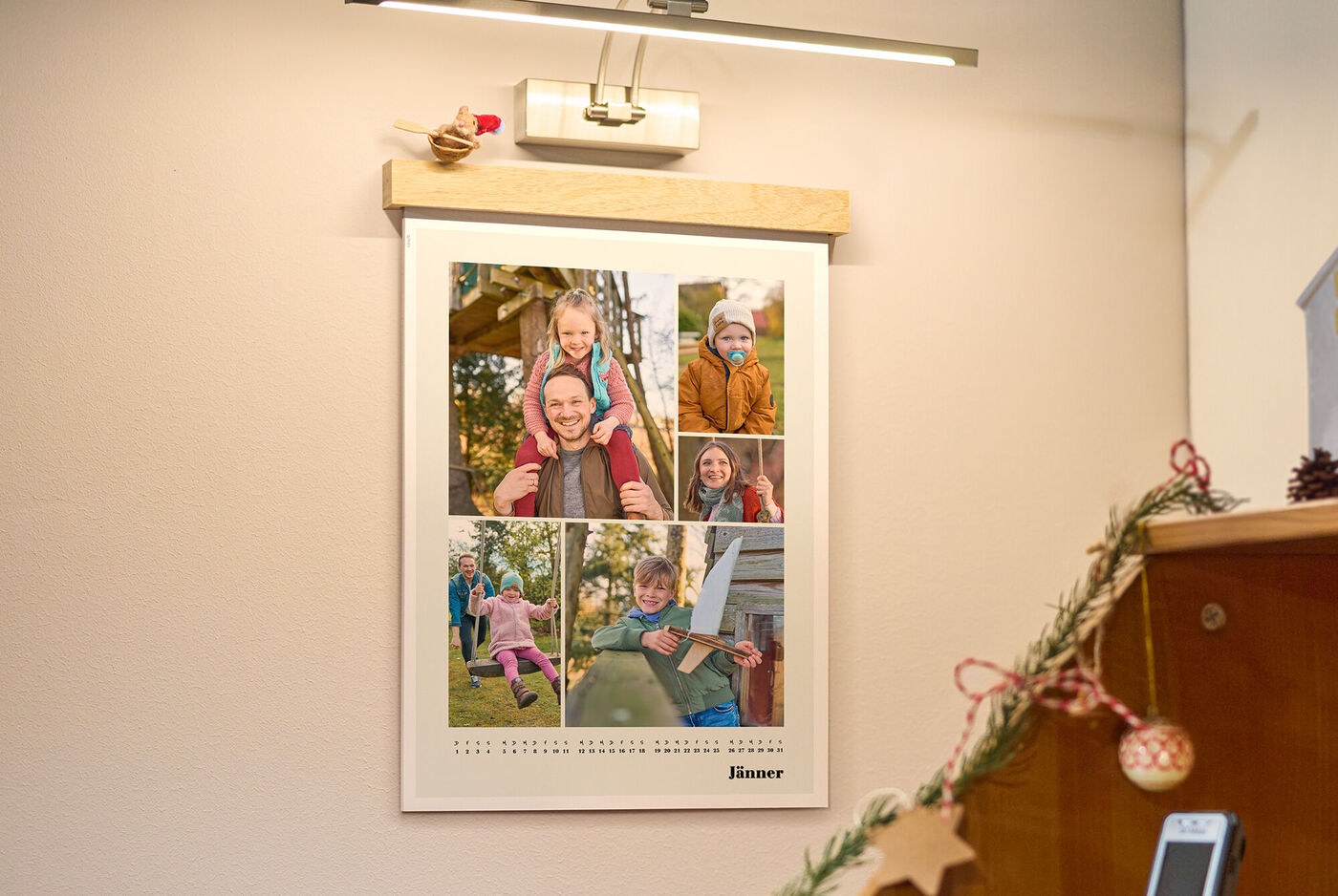 Unter warmem Licht hängt ein Familien-Fotokalender mit fröhlichen Outdoor-Momenten; zarte Weihnachtsdeko daneben – ein Zuhause voller Erinne